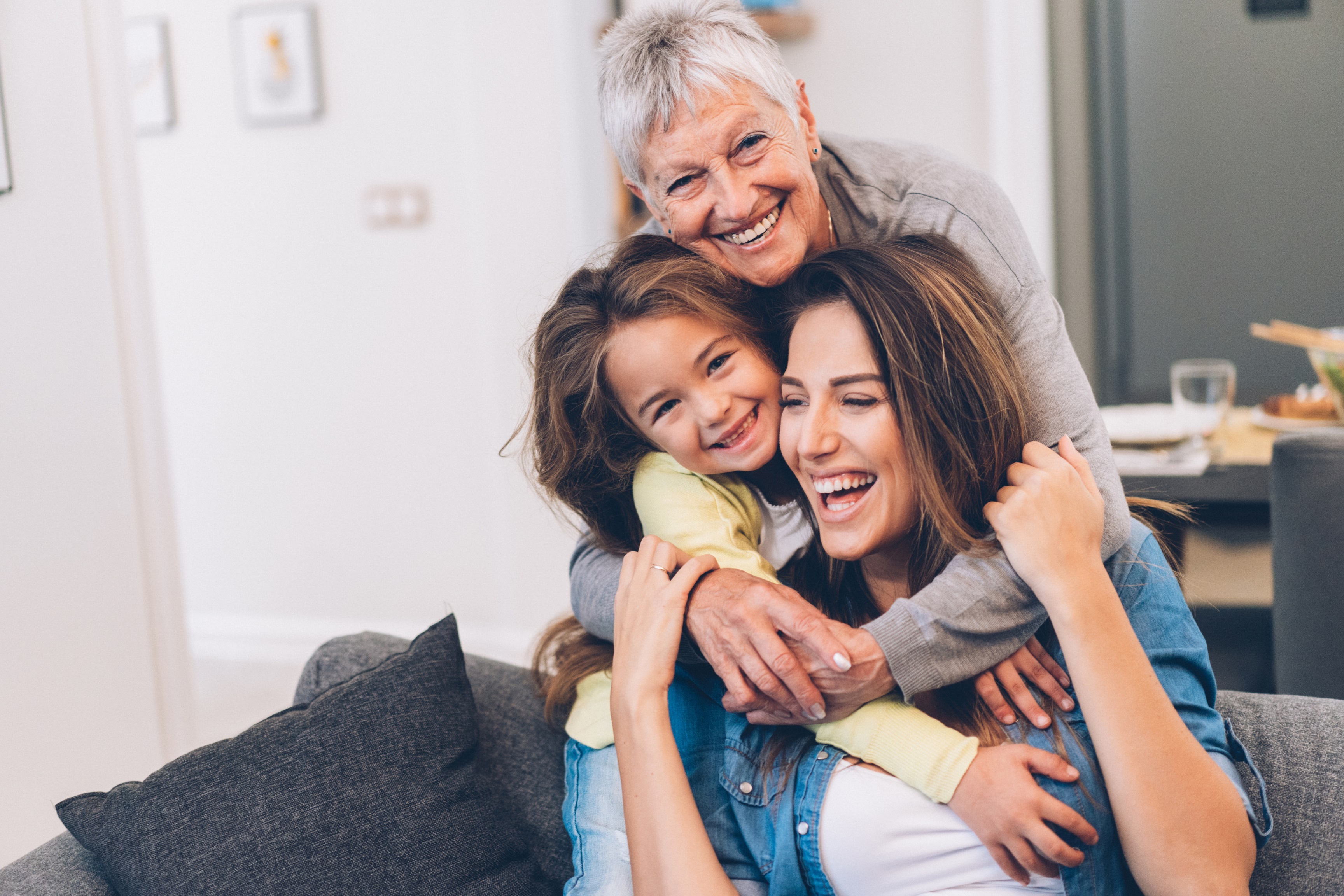 Grandmother, daughter, and granddaughter all hug one another and smile